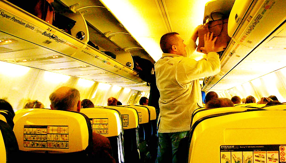 Uomo che metta nella cappelliera il suo bagaglio a mano in un aereo di Ryanair