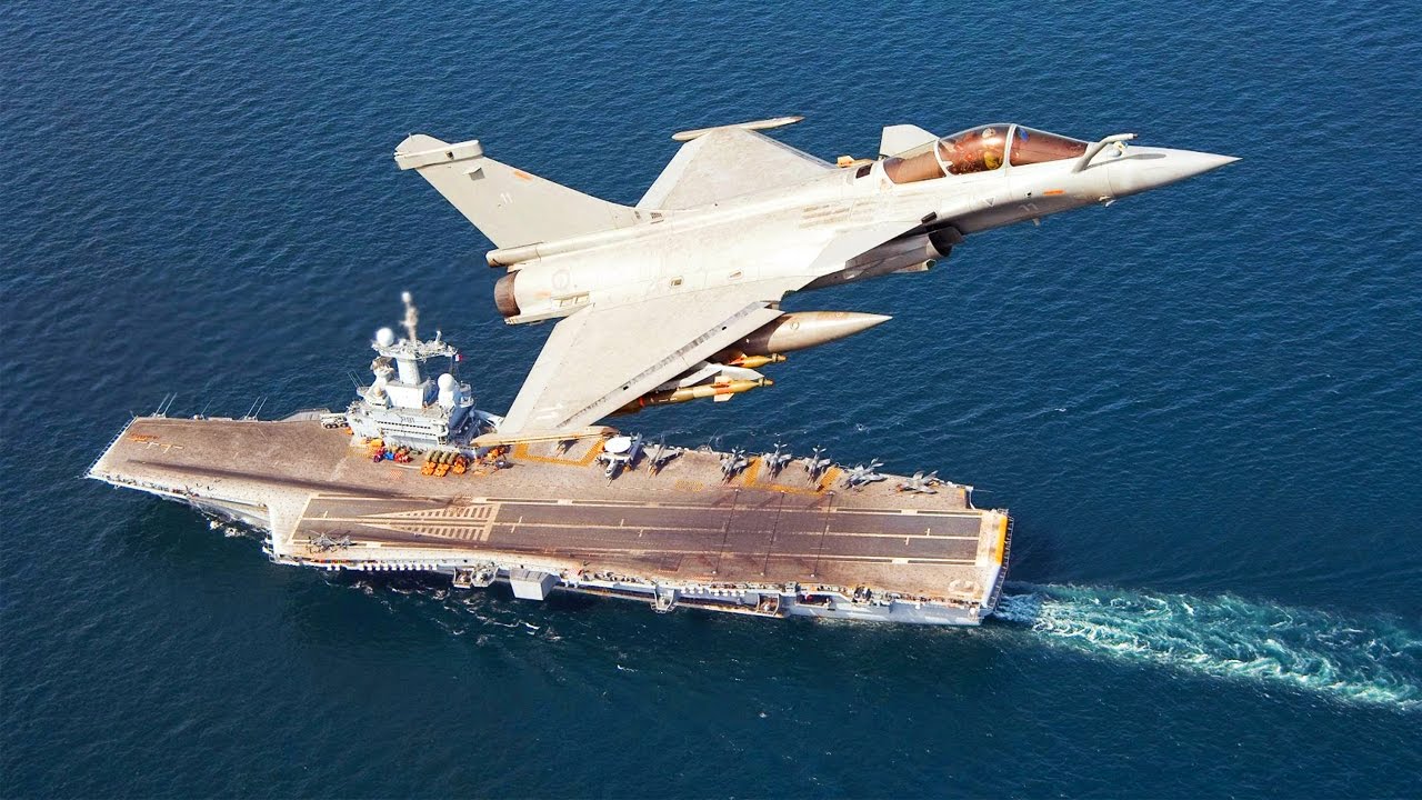 Un aereo Dassault Rafale dell'Aéronautique navale con sullo sfondo la portaerei "Charles de Gaulle"