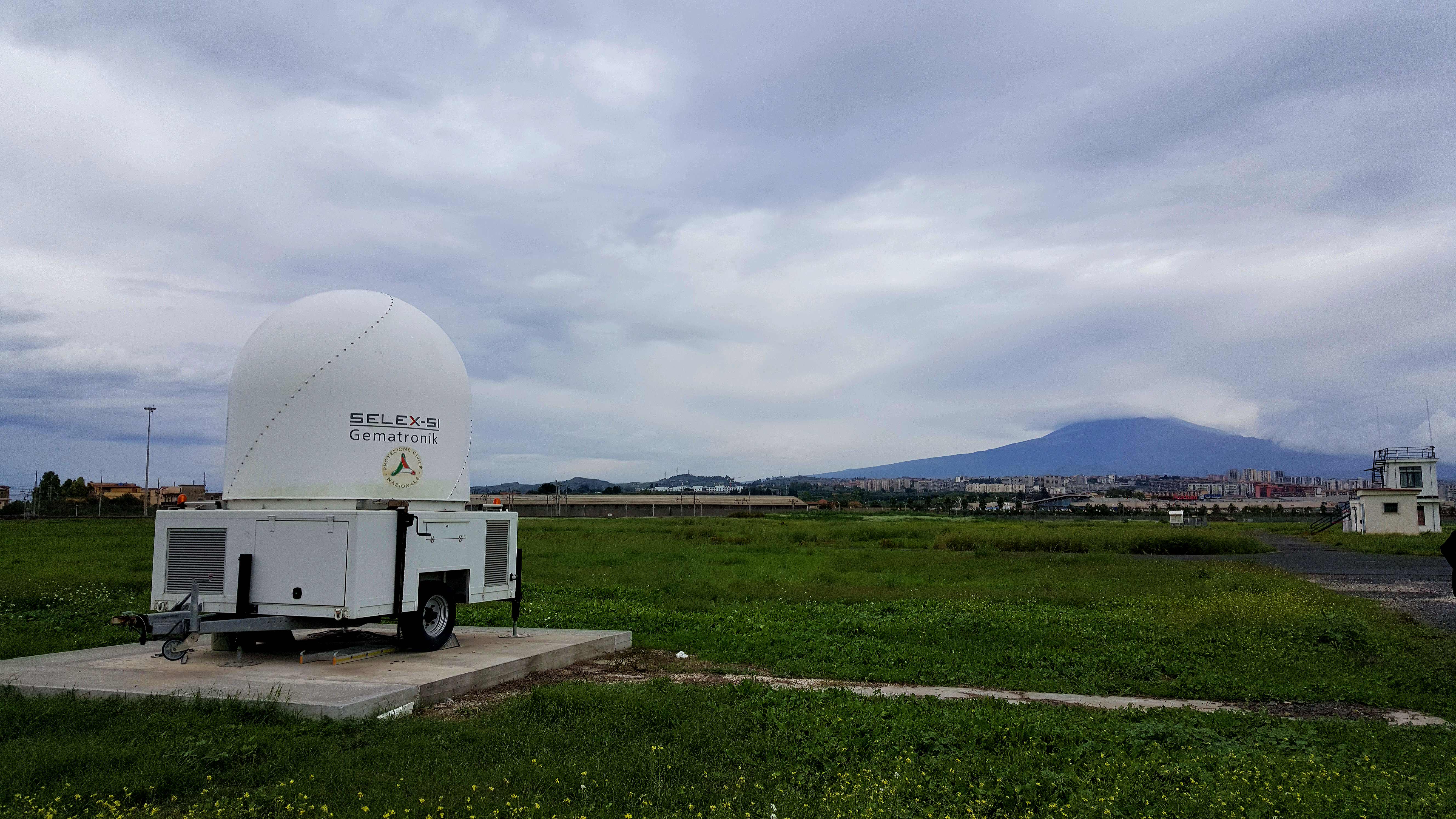 Radar di monitoraggio delle ceneri vulcaniche dell'Etna (sullo sfondo), installato all'Aeroporto di Catania-Fontanarossa dalla Protezione Civile.